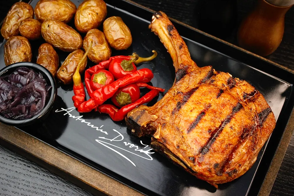 Vepřový tomahawk z grilu na talíři s podpisem Antonína Dvořáka