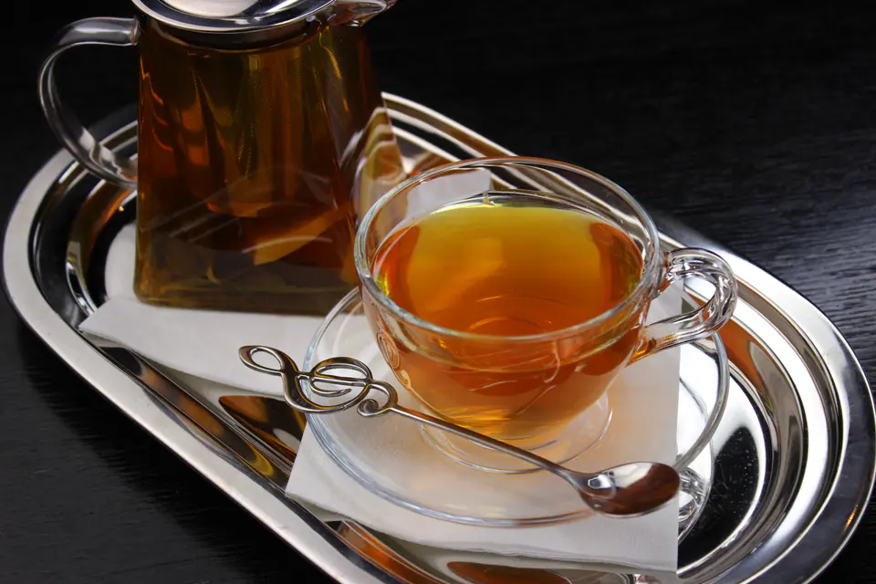 Tea in a glass teapot with a cup on a silver tray