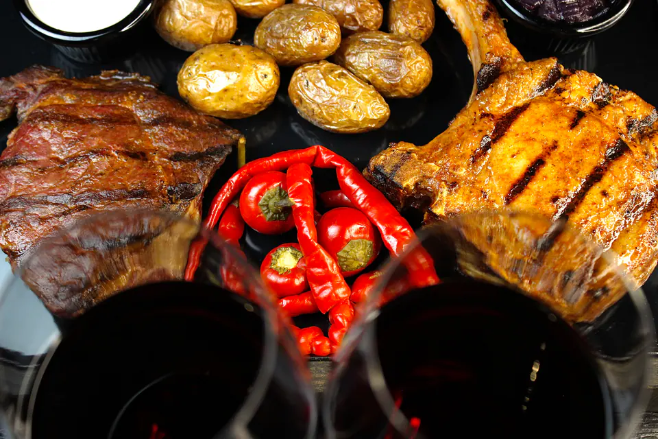 Grilled meat, potatoes and peppers on a board with glasses of wine