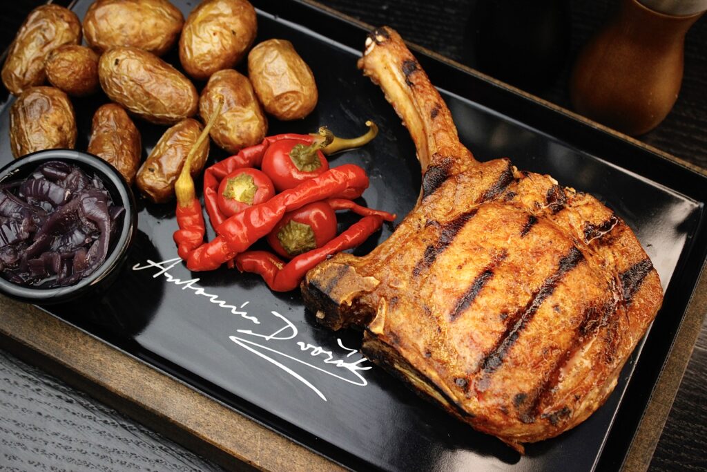Grilovaný steak Tomahawk s pečenými bramborami, nakládanými papričkami a červeným zelím podávaný v restauraci A. Dvořák Praha.